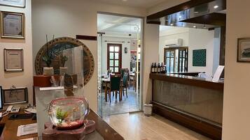 A hotel lobby with a reception desk, framed certificates on the wall, a decorative fish bowl, and a view into the dining area.