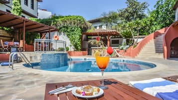 A poolside dining area with a table set for two, a glass of orange juice, and a plate of food.