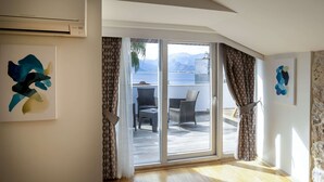 Una habitación con un amplio ventanal corredera que da a un espacio exterior con mobiliario de mimbre y vistas a montañas.