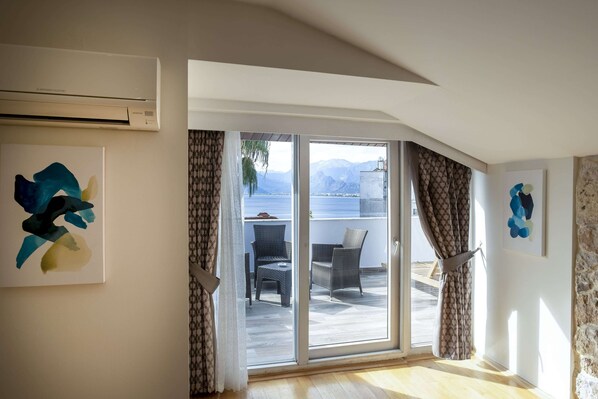 Una habitación con un amplio ventanal corredera que da a un espacio exterior con mobiliario de mimbre y vistas a montañas.