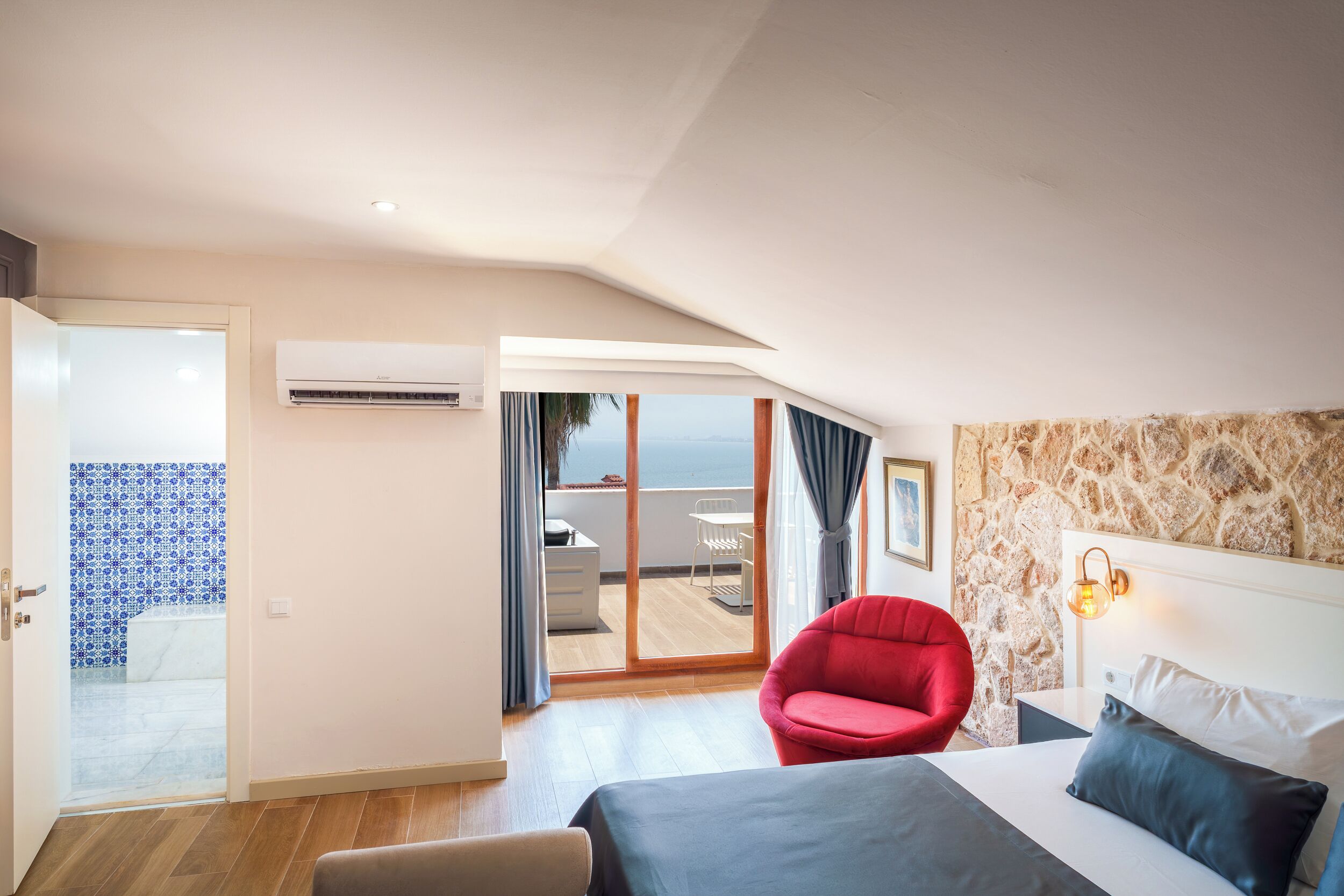 Hotelkamer met een bed, een rode stoel, een badkamer met een blauw patroon gedoucheruimte en een balkon met uitzicht.