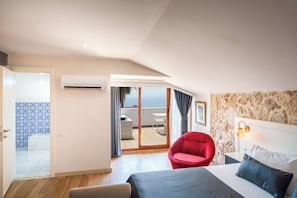 Habitació d'hotel amb un llit, una cadira vermella, un bany amb dutxa de disseny blau i un balcó amb vistes.