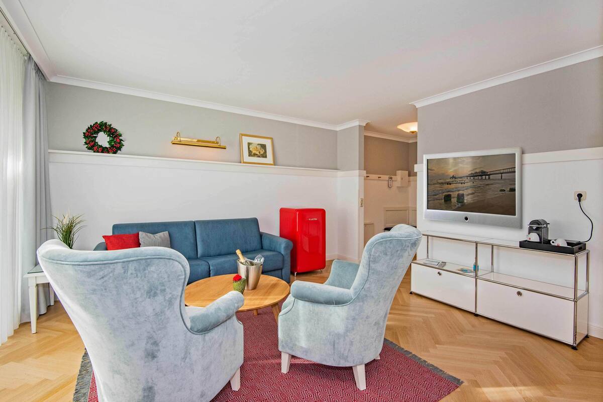 Ein modernes Wohnzimmer mit einem blauen Sofa, zwei grauen Sesseln, einem Holztisch und einem roten Schrank.
