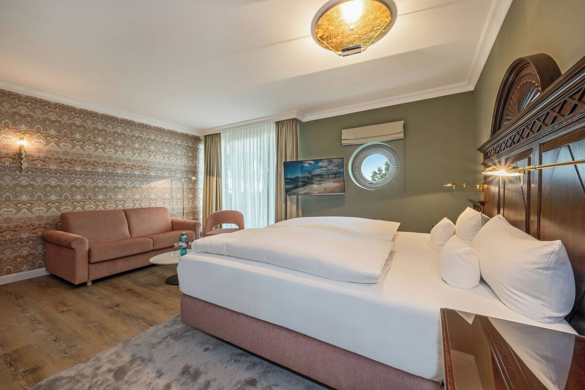 Ein Hotelzimmer mit einem großen Bett, einer Couch, einem kleinen Tisch und einem Fernseher.