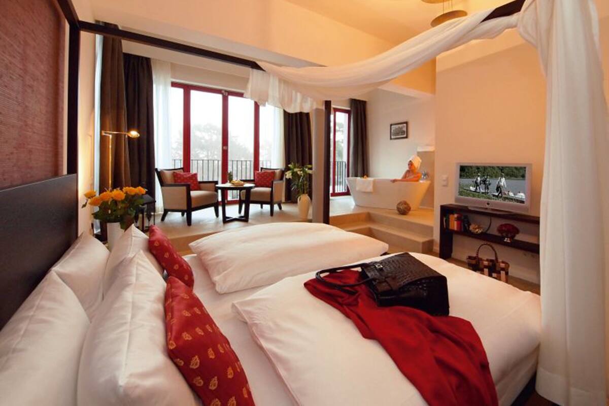 Ein Hotelzimmer mit einem großen Bett, einer Sitzecke mit Tisch und Stühlen, einer Badewanne und einem Fernseher auf einem Schrank.