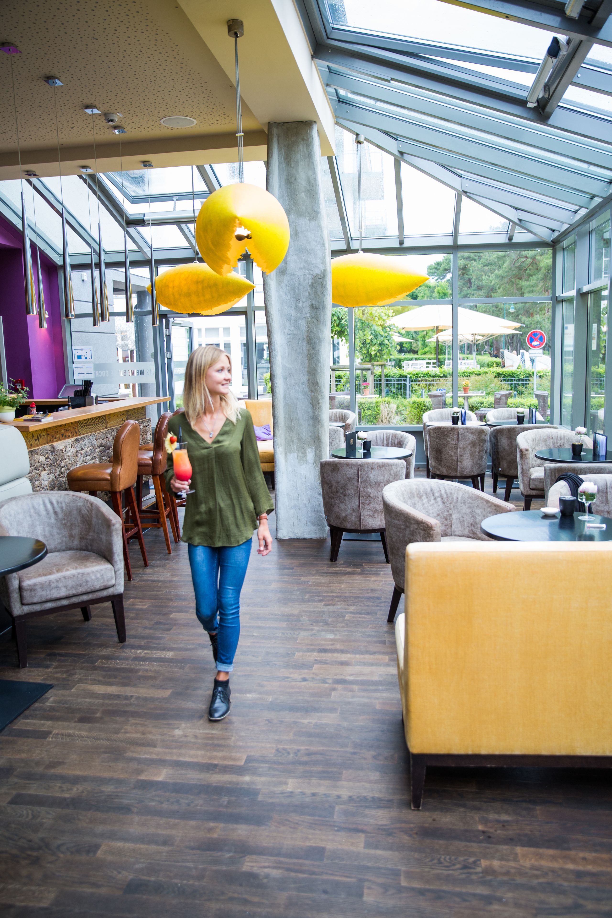 A modern indoor space with a glass ceiling, wooden flooring, and yellow upholstered seating.