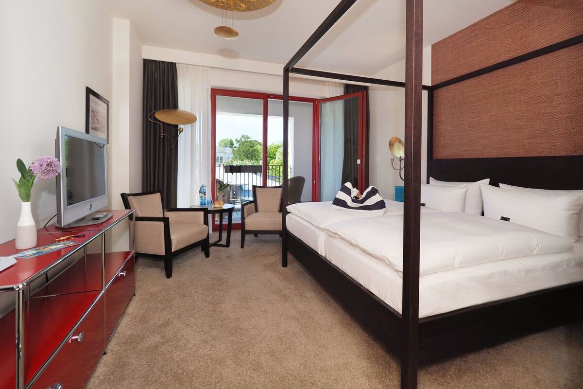 Ein Bett mit Baldachin, ein Fernseher, ein Schreibtisch mit Stuhl und Blick ins Freie.