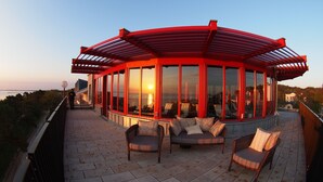 A covered outdoor seating area with a view of the sunset over the water.
