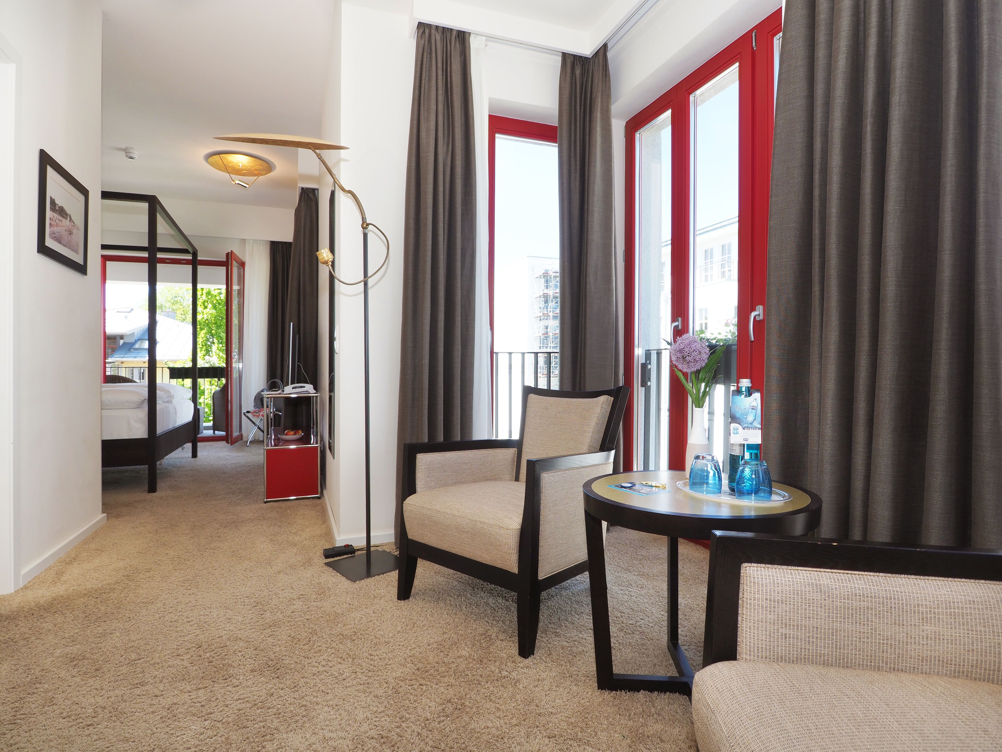 A hotel room with a bed, a chair, a small table, and a window with curtains.