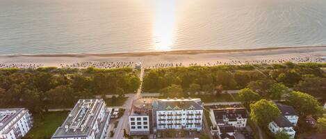 Vista aérea de una zona costera con una playa, una hilera de edificios blancos con balcones y un estacionamiento.
