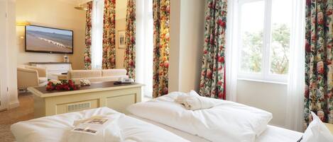 Habitación de hotel con dos camas, un escritorio, un televisor y cortinas estampadas.