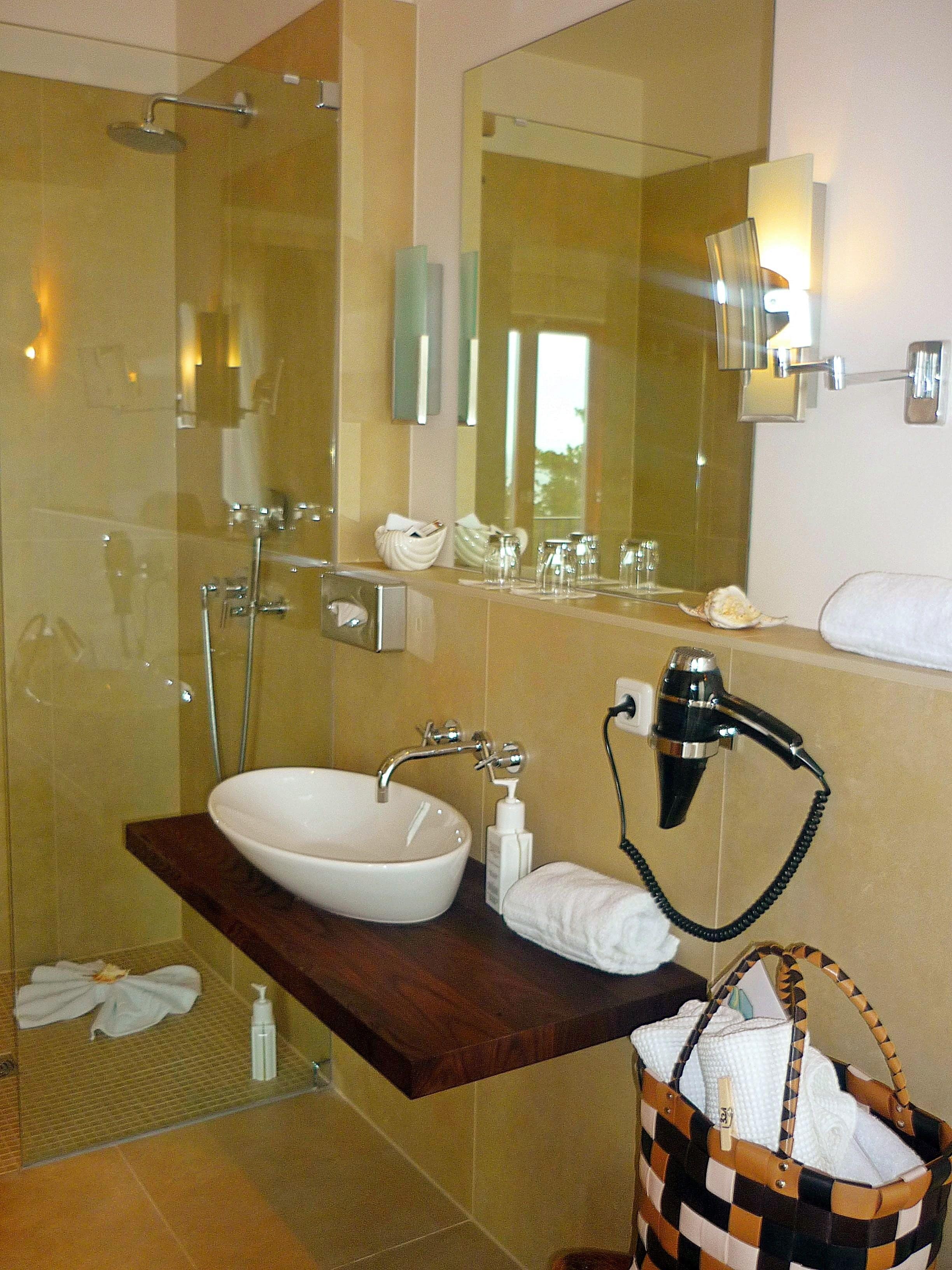 A bathroom with a glass shower enclosure, a white sink, a towel rack, and a hairdryer on the counter.