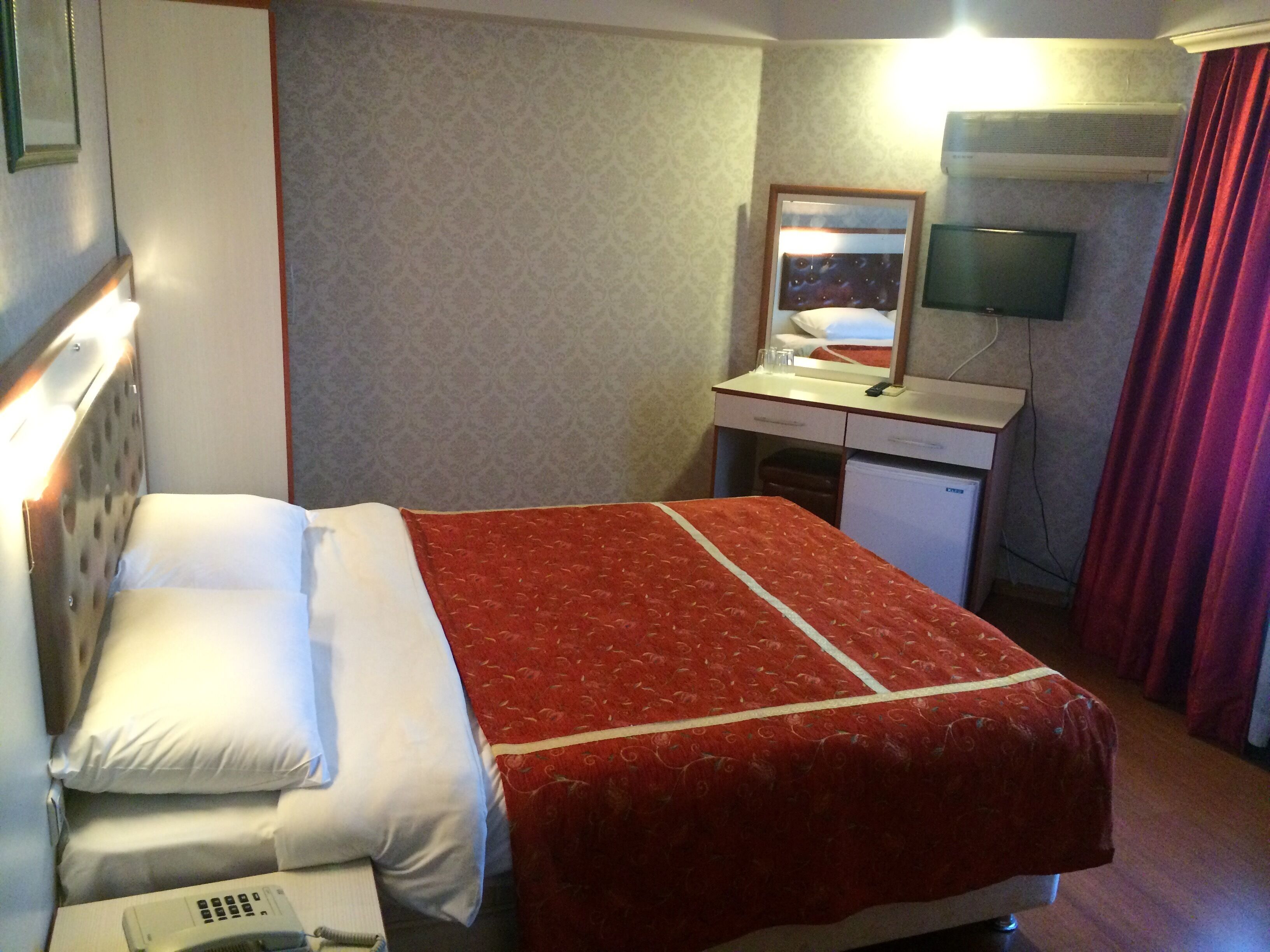 A hotel room with a bed, a desk, a mirror, a television, and a red curtain.