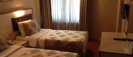A hotel room with two beds, a bedside table with a lamp, a TV, and a window with curtains.