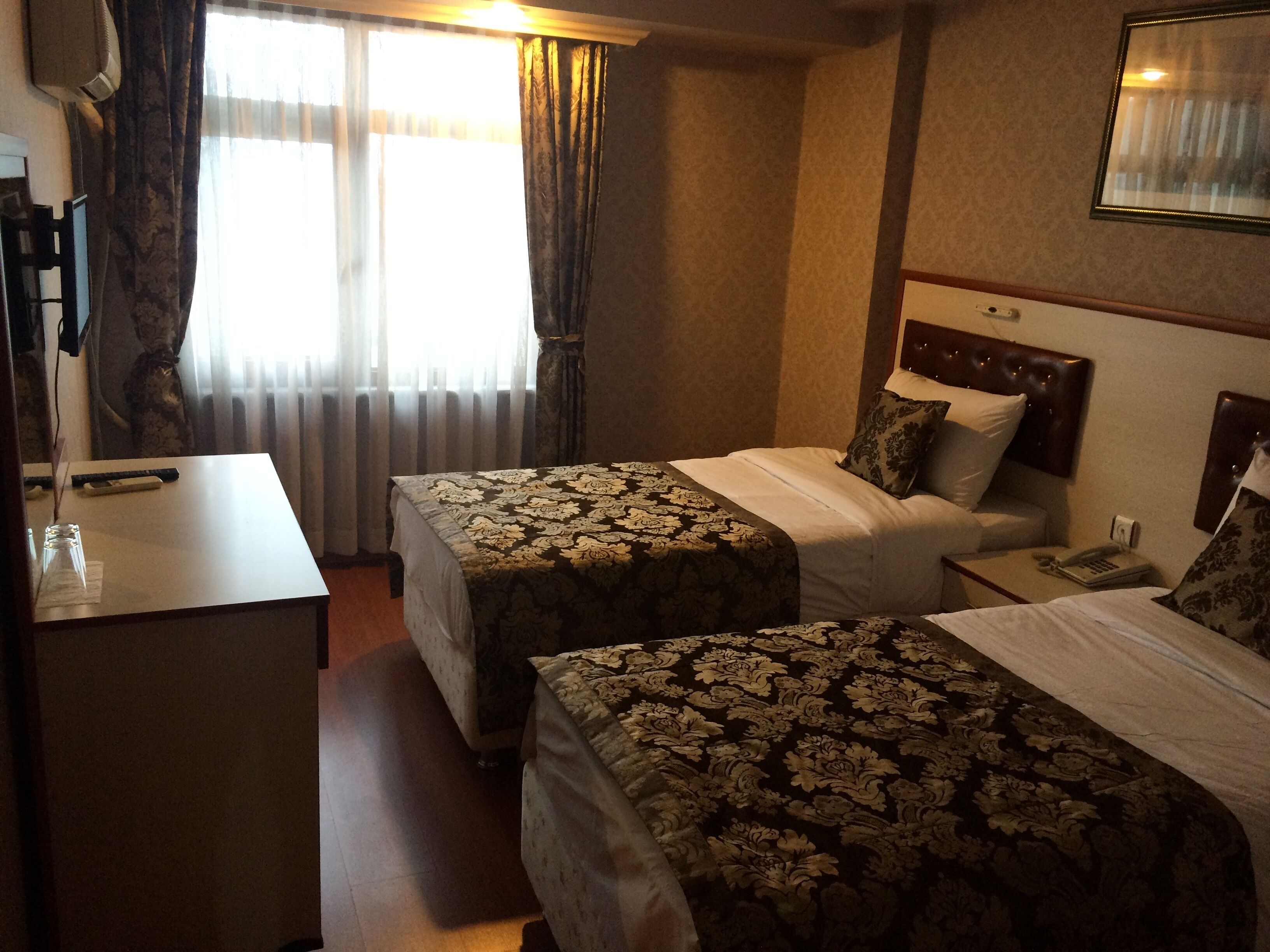 A hotel room with two beds, a desk, and a window with curtains.