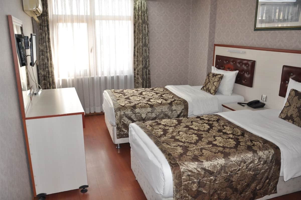 Hotellihuone, jossa on kaksi sänkyä, työpöytä ja ikkuna, jossa on verhot.