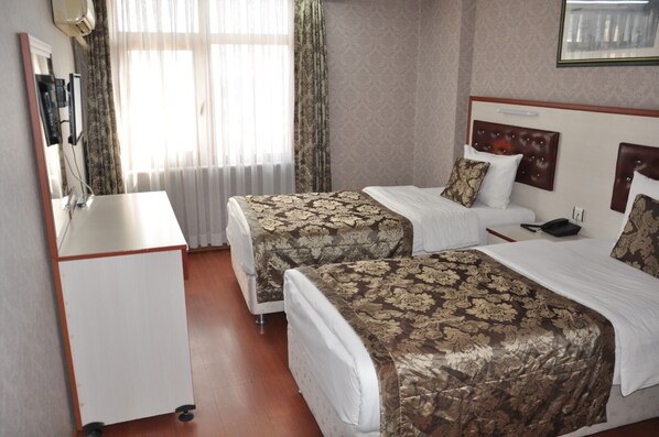 Een hotelkamer met twee bedden, een bureau en een raam met gordijnen.