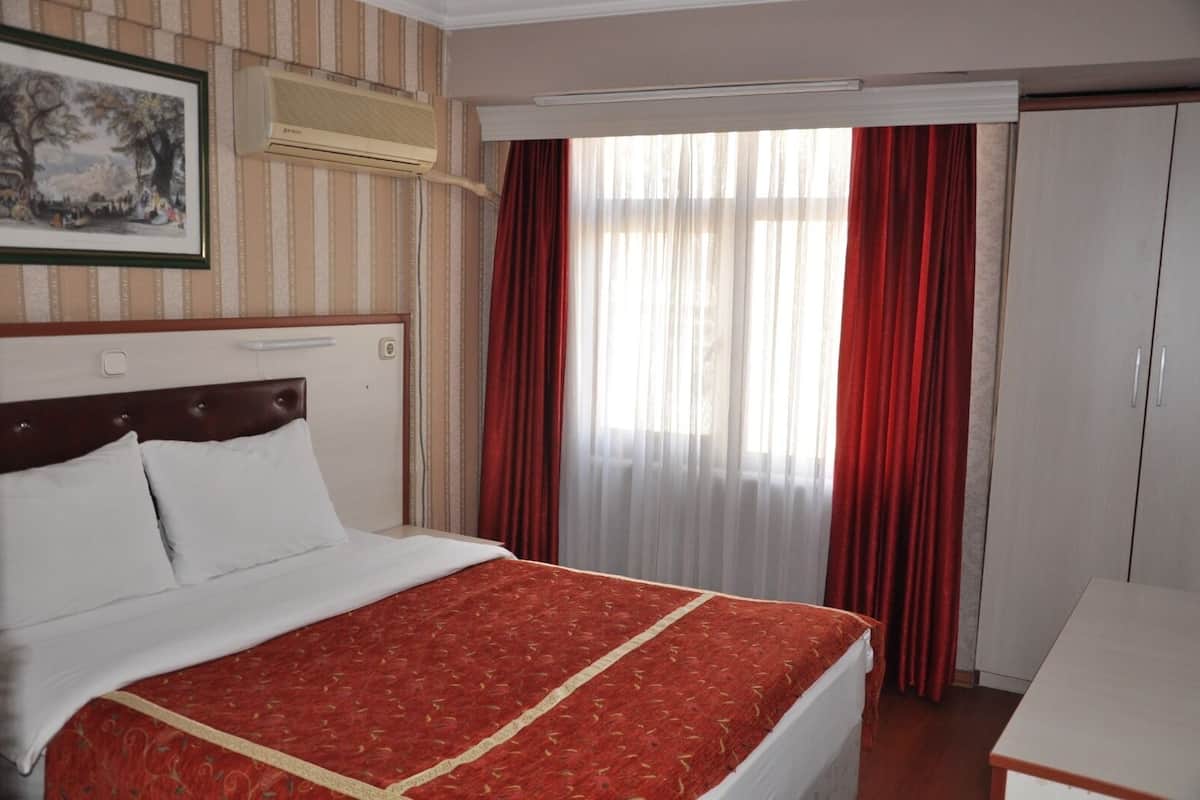 Hotellihuone, jossa on suuri sänky, yöpöytä, vaatekaappi ja ikkuna, jossa on verhot.