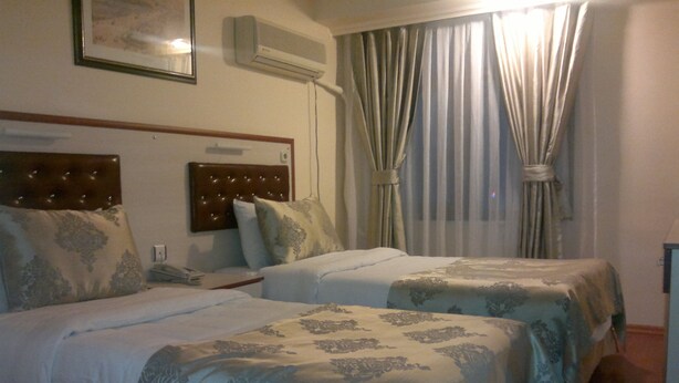 A hotel room with two beds, a headboard, a bedside table, a lamp, and a window with curtains. - Tayhan Hotel (Istanbul)