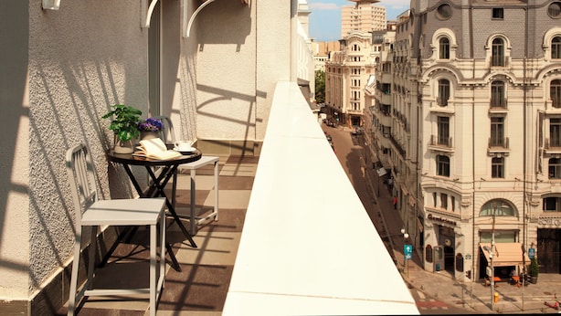 A narrow balcony with a white table and chair, a potted plant, and a view of adjacent buildings. -  Zeus Essence Bucharest, Trademark Collection by Wyndham (Bucharest)