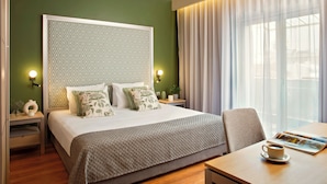 A neatly arranged hotel room with a large bed, a bedside table with a lamp, a chair, and a table with a cup and a magazine. -  Zeus Essence Bucharest, Trademark Collection by Wyndham (Bucharest)