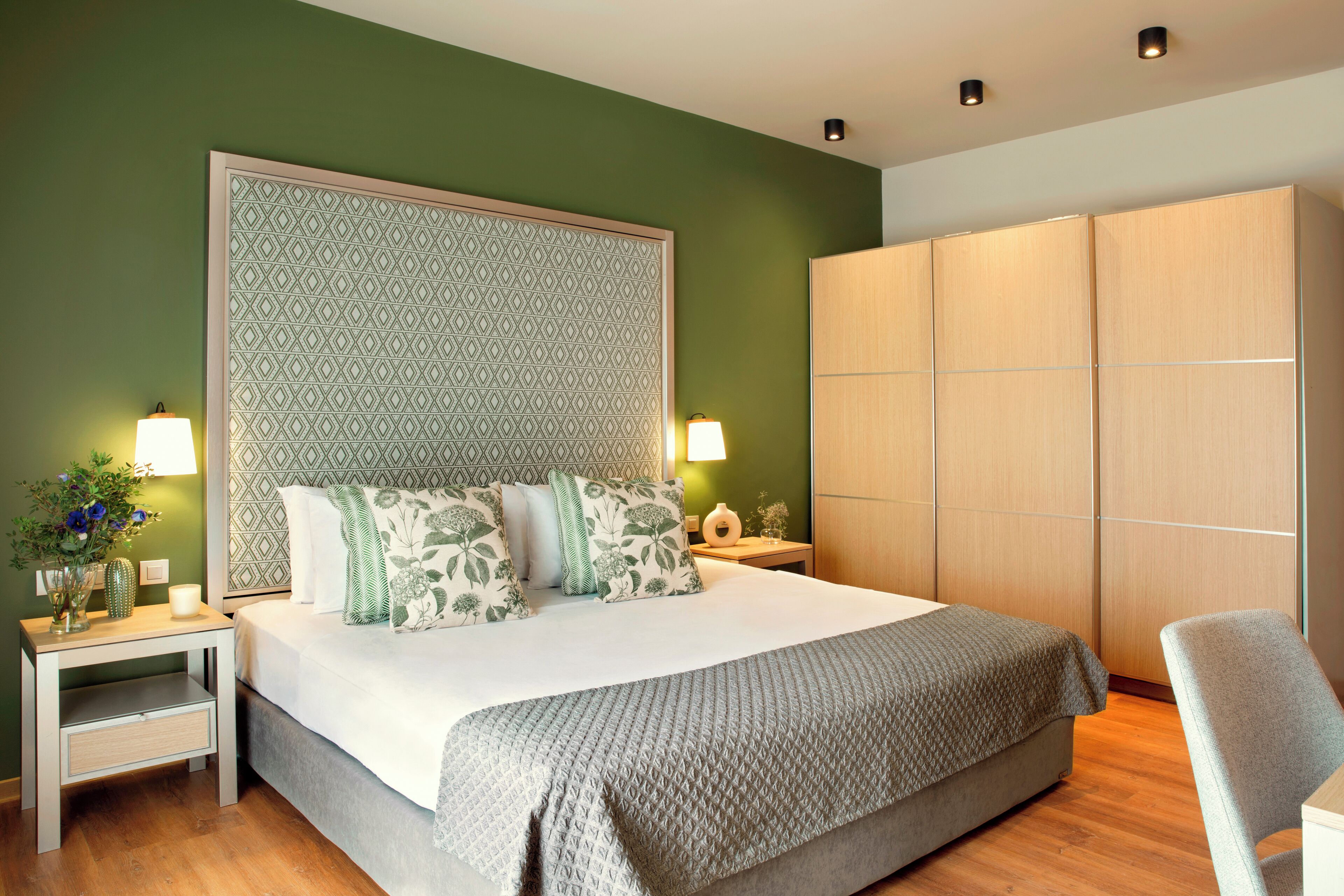 A neatly arranged bedroom with a large bed, a nightstand with a lamp, a dresser, and a chair.