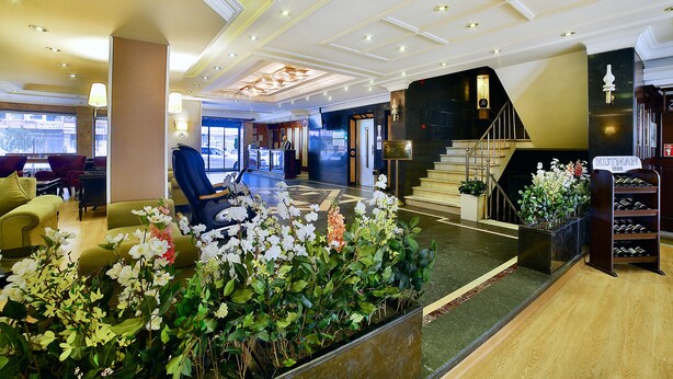 A hotel lobby with a reception desk, seating area, staircase, and a display of wine bottles. - Hotel Grand Emin (Istanbul)