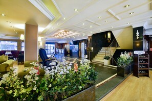 Un vestíbulo de hotel con mostrador de recepción, zona de estar, escalera y exhibición de botellas de vino.