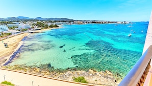 A coastal view with clear turquoise waters, a sandy beach, and a backdrop of buildings and hills. - NYX Hotel Ibiza - Adults Only (Sant Antoni de Portmany)