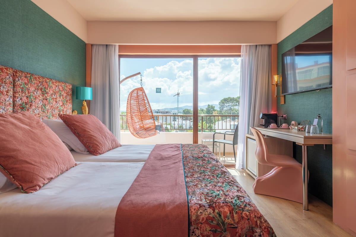 Habitación de hotel con cama, escritorio, silla y una mecedora, con vista al exterior.