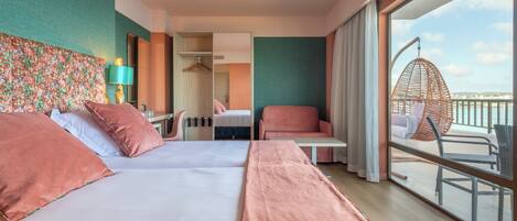 A hotel room with two beds, a sitting area with a chair and table, a large window with a view, and a mirror.
