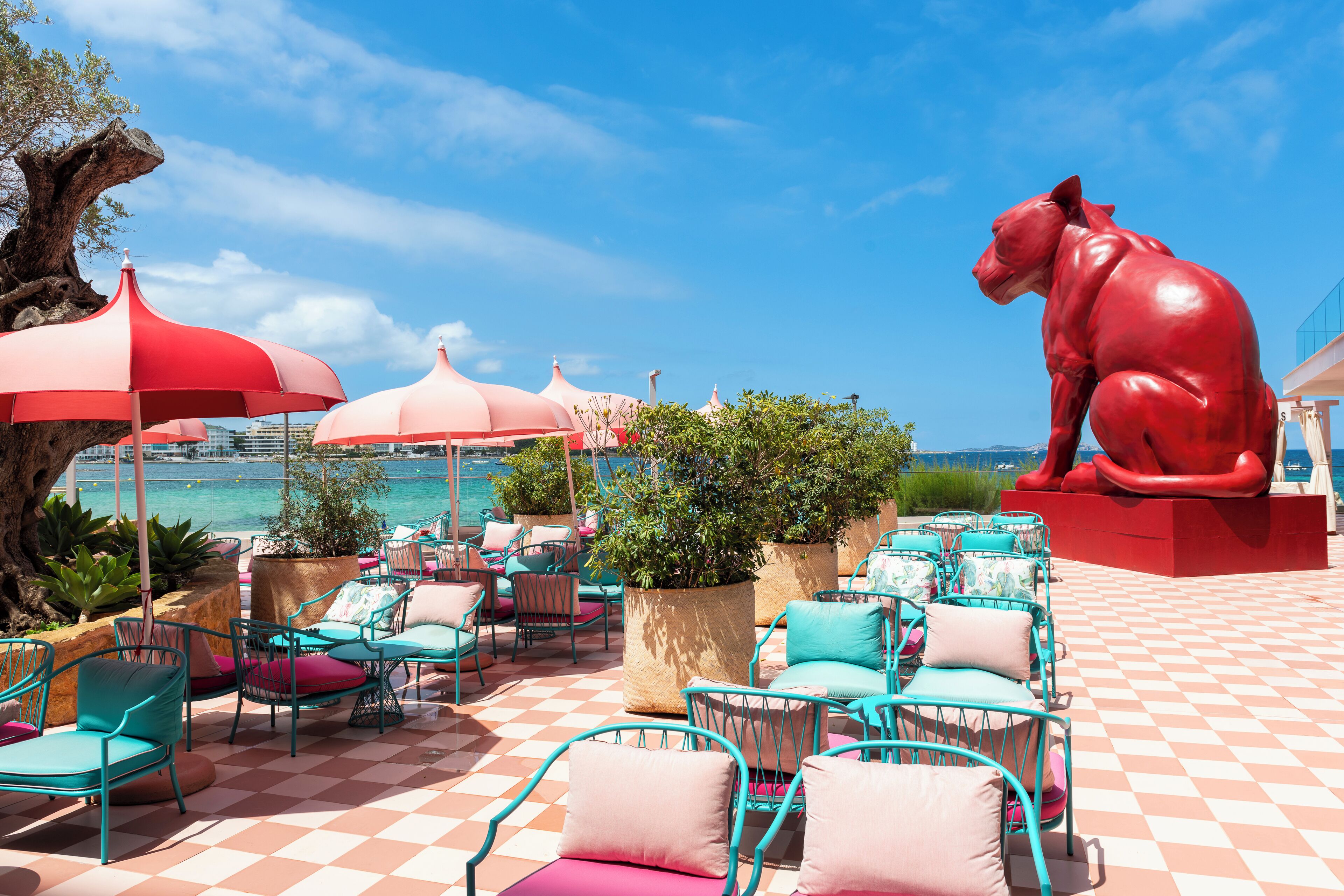 Une terrasse dotée d’un sol à carreaux, de sièges extérieurs et d’une grande sculpture rouge.