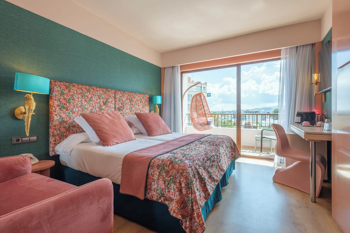 Habitación de hotel con cama, escritorio, silla, balcón y una hamaca colgante.