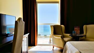 Habitación de hotel con cama, dos sillones, una mesita, televisor y un ventanal con vista al océano.