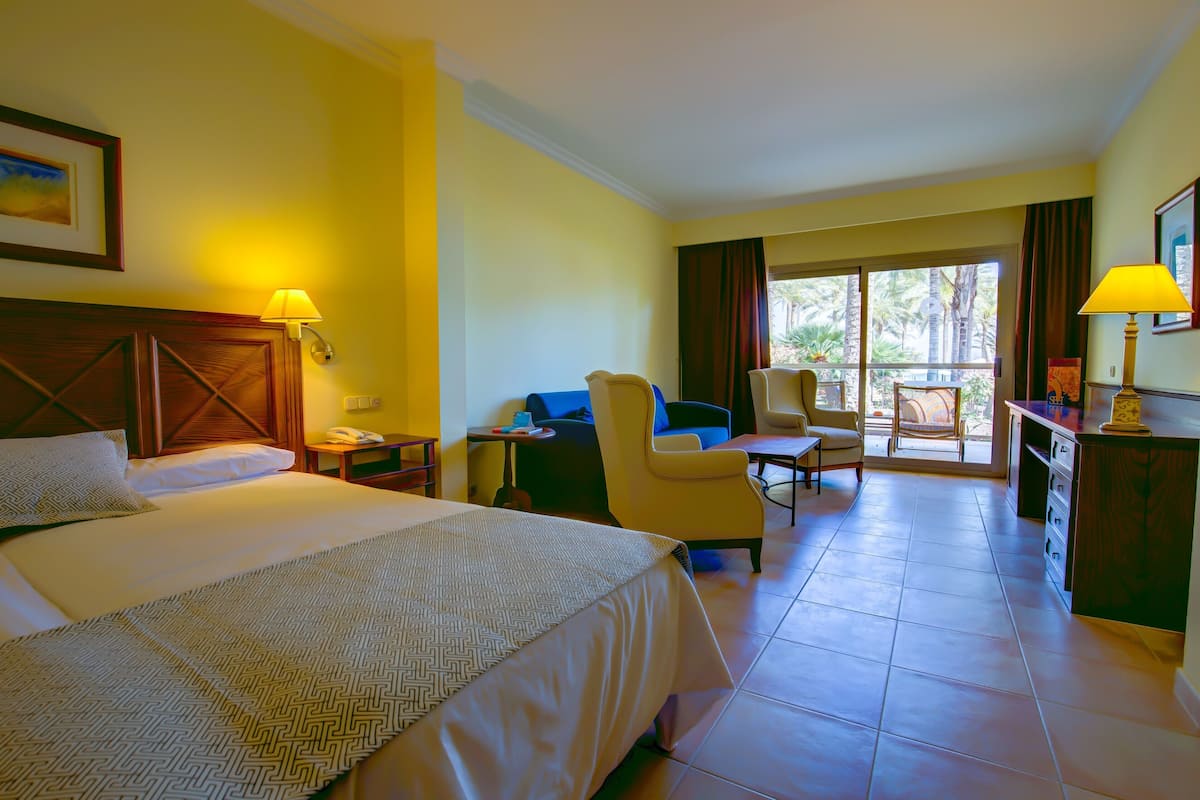 A hotel room with a large bed, a desk, a chair, and a balcony with a view.