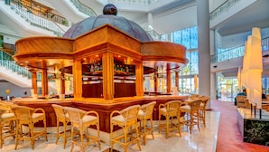 Un amplio atrio con una zona de bar central, sillas de mimbre y una estructura abovedada decorativa.