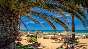 Una playa con palmeras, sillas de descanso y sombrillas.
