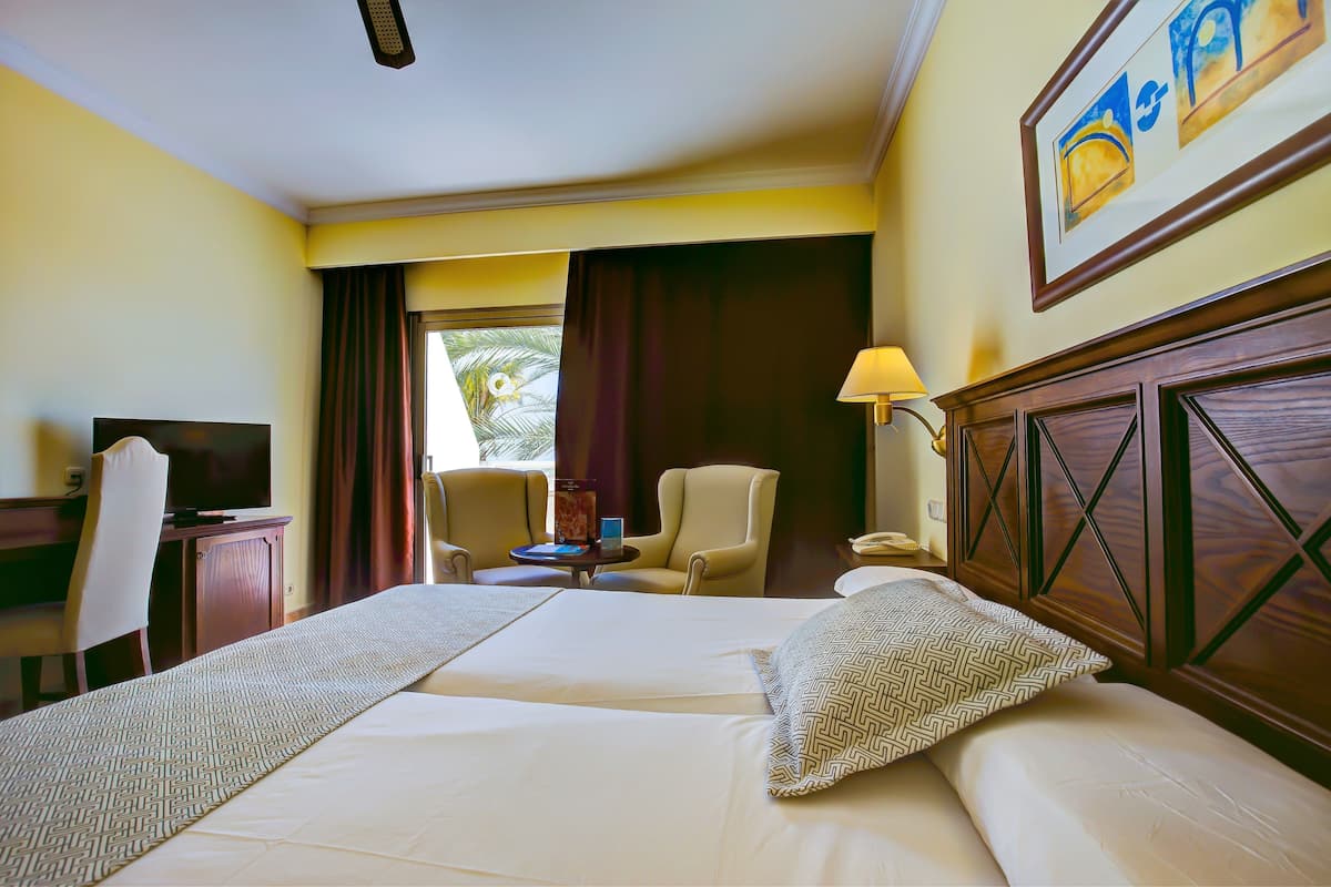 A hotel room with a large bed, a desk with a television, a chair, a lamp, and a window with curtains.
