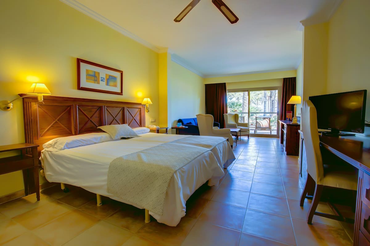 A hotel room with a large bed, two bedside tables, a desk with a chair, a television, and a window with curtains.