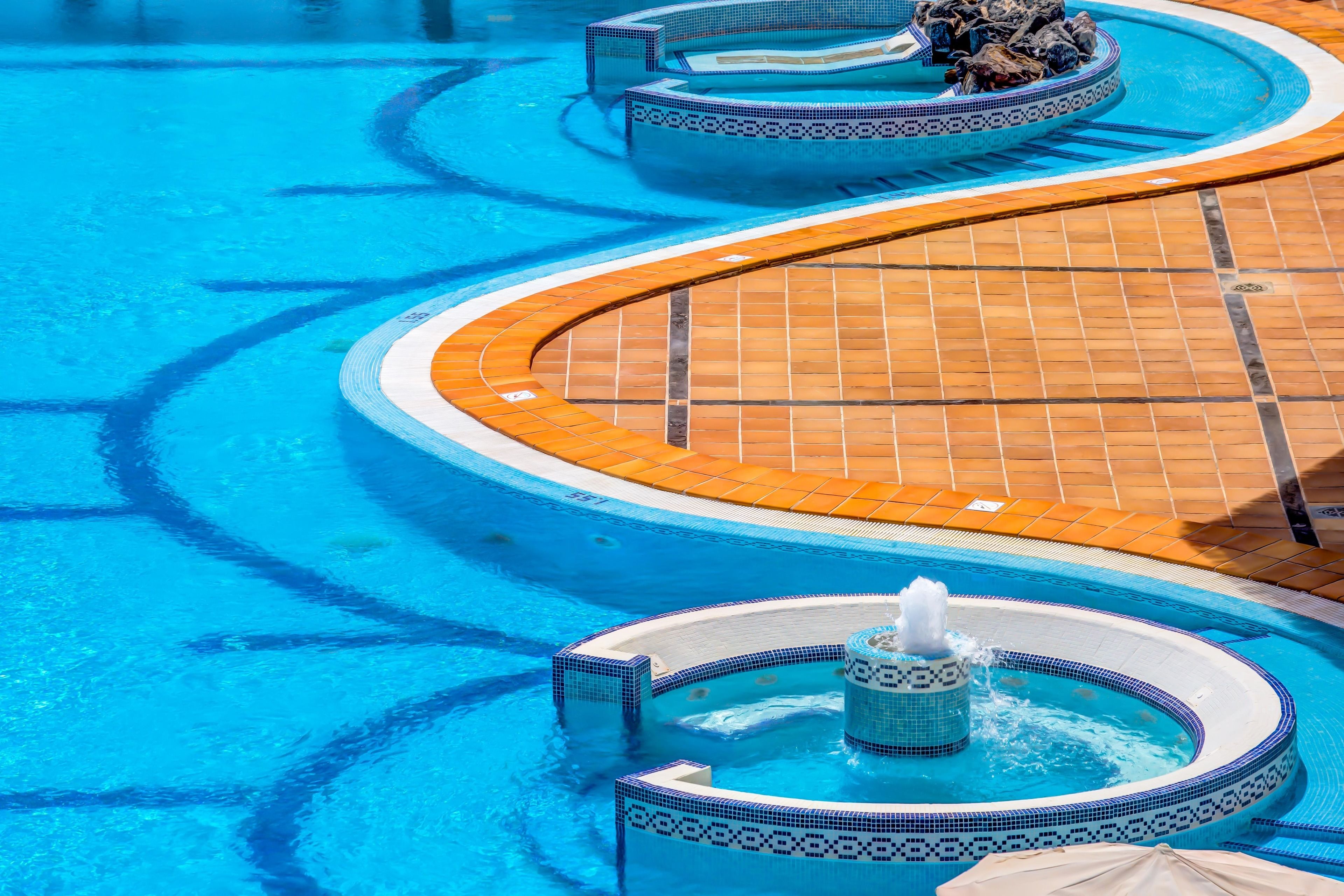 A swimming pool with a tiled deck and a hot tub area.