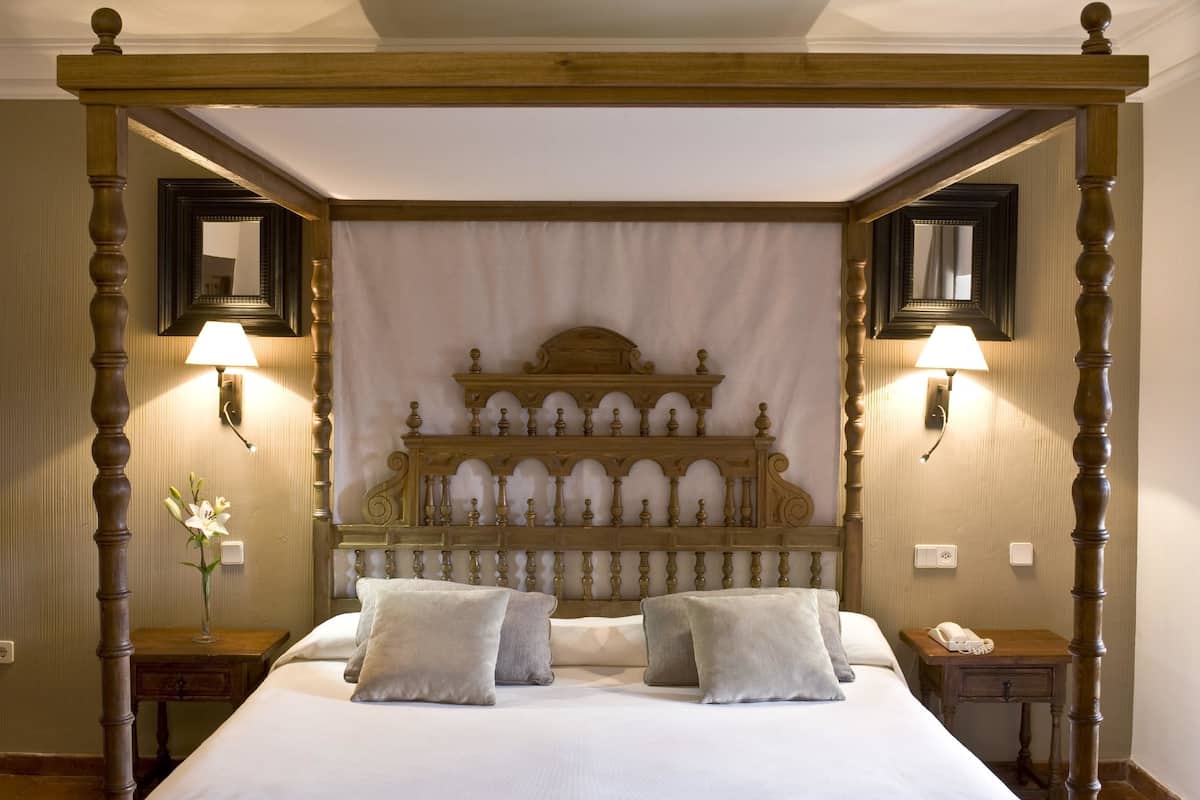 Ein Himmelbett mit massivem Holzkopfstück, zwei Nachttischlampen und ein Nachttisch mit Telefon.