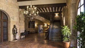 Un vaste hall doté d’un sol en pierre, d’un grand lustre et d’un escalier menant à un niveau supérieur.