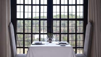 A dining table set for two with a view of a forest through a large window with a grid pattern.