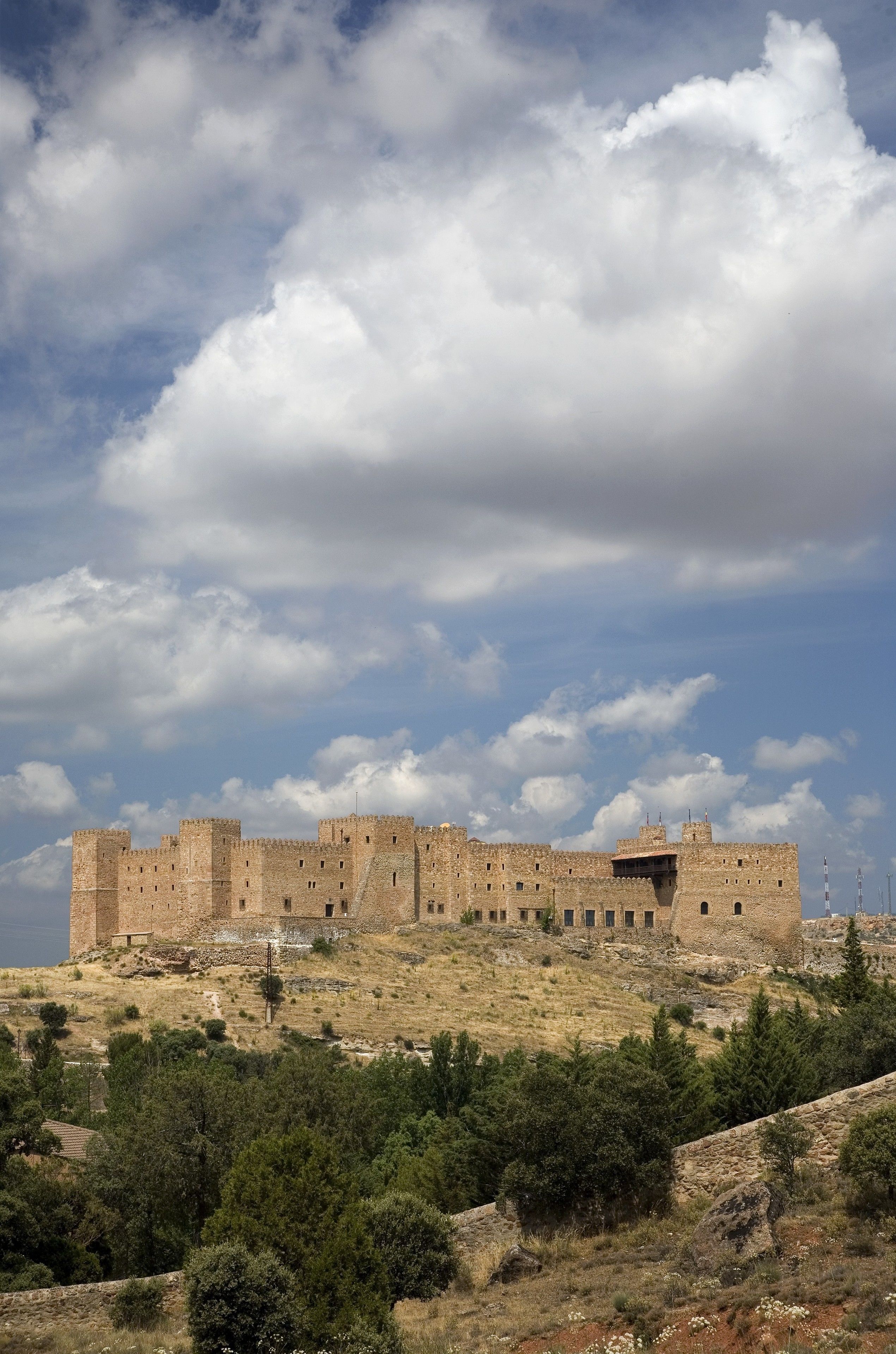 A historic stone castle with multiple towers, situated on a hill with sparse vegetation.