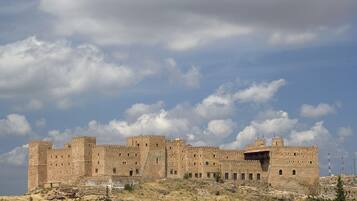 A historic stone castle with multiple towers, situated on a hill with sparse vegetation.