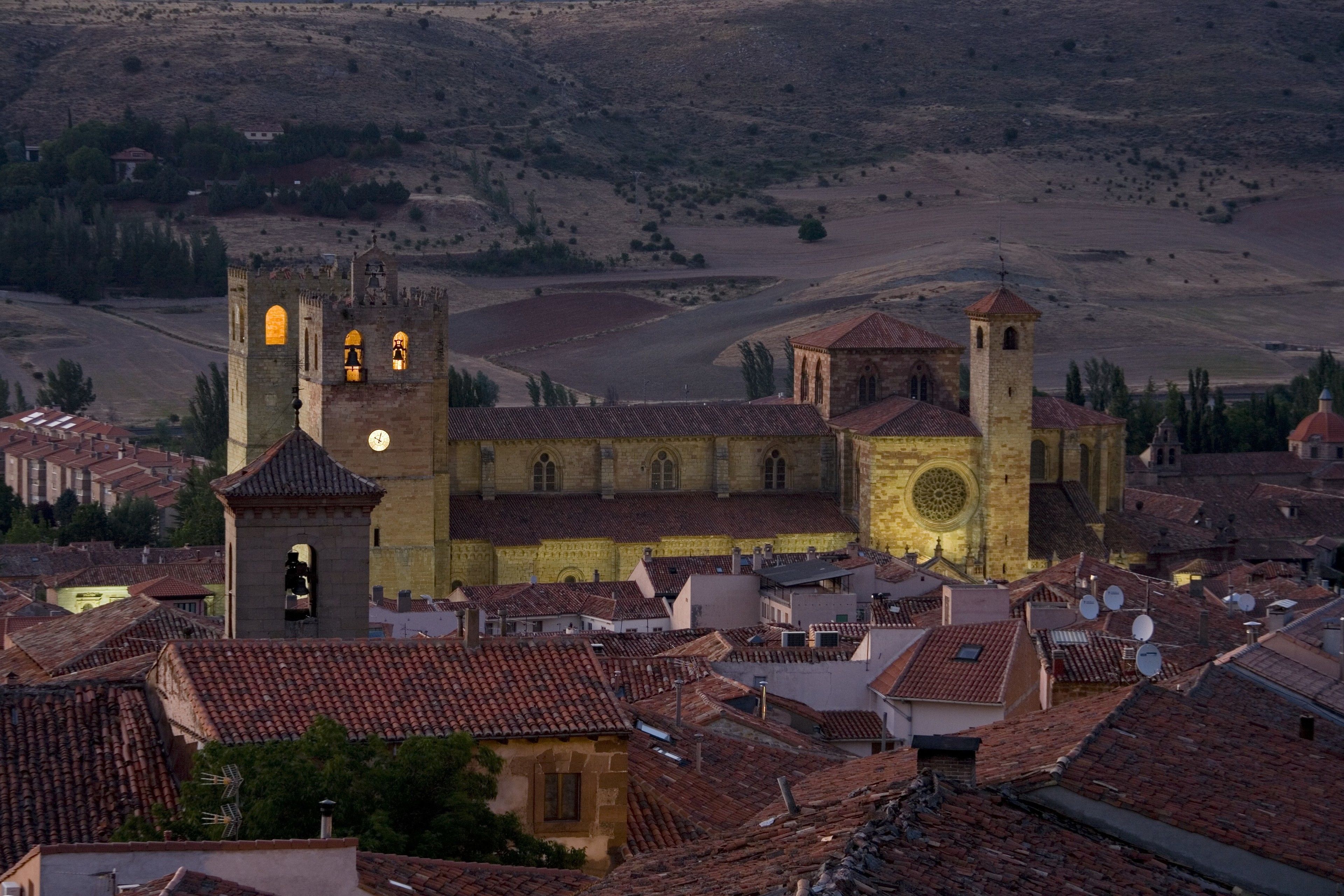 A historic church with a bell tower and a large circular window, surrounded by traditional buildings with red-tiled roofs.