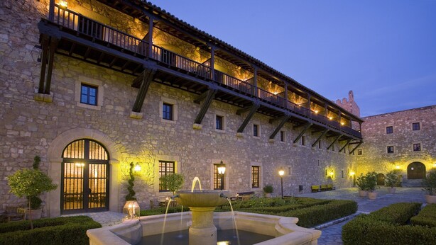 Un bâtiment en pierre doté d’une cour, d’une fontaine et d’un balcon illuminé.