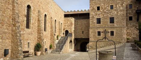 A courtyard with stone buildings, a staircase, and a fountain.