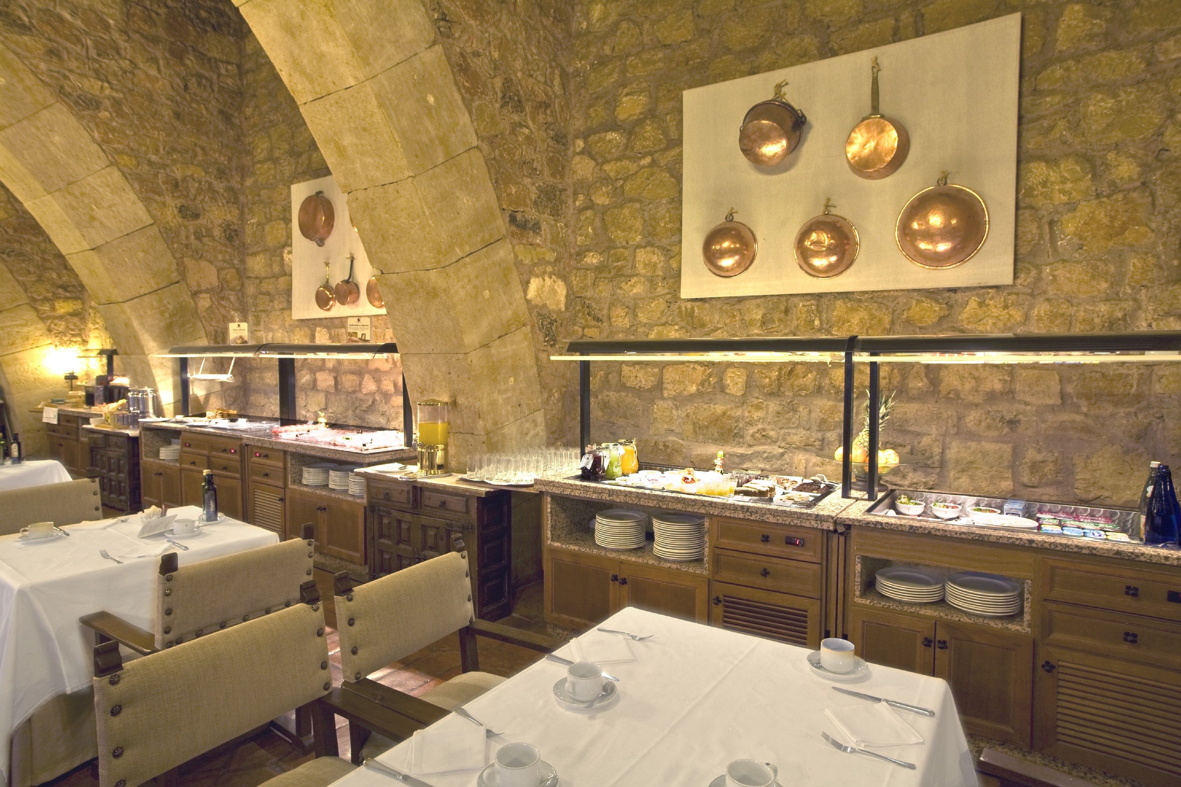 Un restaurante con paredes de piedra, varias mesas preparadas para comer y una variedad de platos expuestos en la barra.