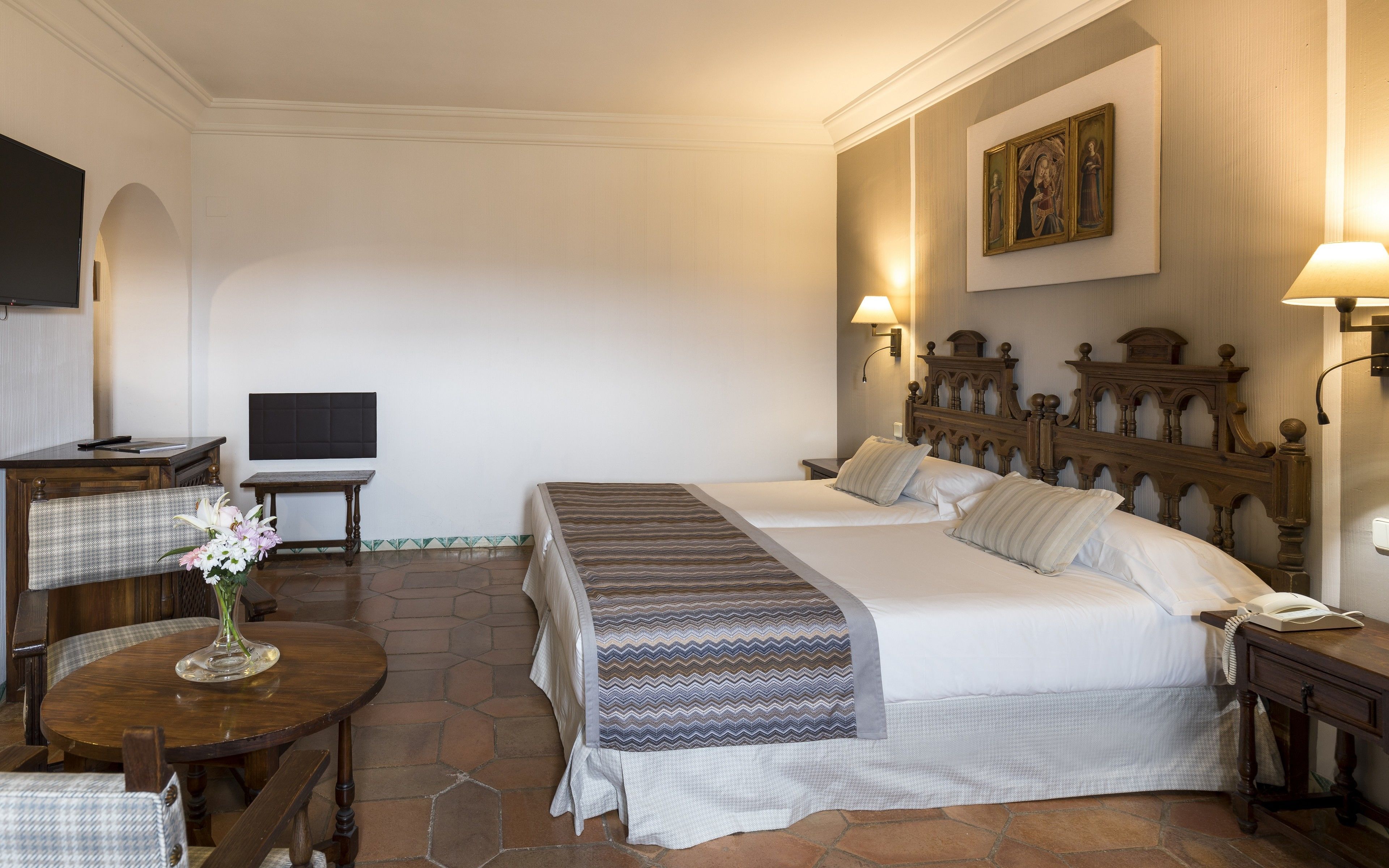 A hotel room with two beds, a desk, a chair, a TV, and a painting on the wall.